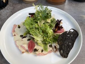 Vitello Tonnato mit Brotchip, dessen Farbe vom Tintenfisch stammt.